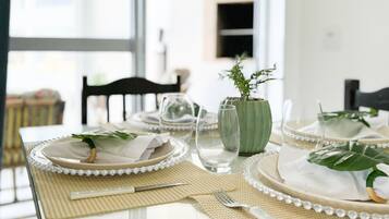 Una mesa de comedor dispuesta con platos blancos, vasos transparentes y un jarrón verde con una planta.