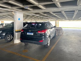 Uma garagem de estacionamento com um SUV preto estacionado perto de um pilar, teto de concreto e uma placa indicando '706-B BOX 069'.