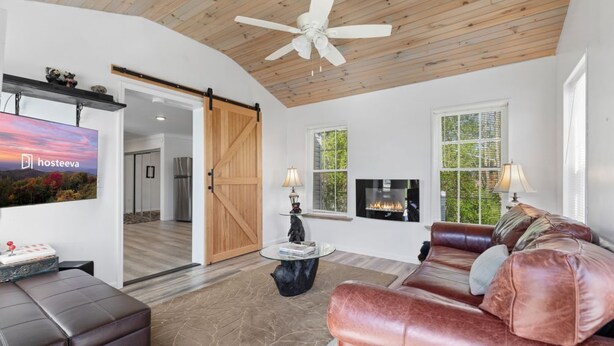 A modern living room with a fireplace, leather sofas, a ceiling fan, and a sliding barn door.
