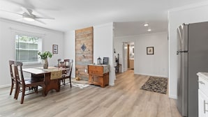 A spacious dining area with a wooden table and chairs, a ceiling fan, and a view into the kitchen.