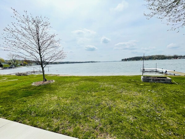 A grassy area with a dock extending into a calm lake, surrounded by trees and a clear sky.