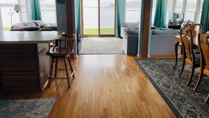 A cozy living room with a large window, a dining area, and a kitchen. - Comfortable 3-bedroom lake house with AC, WiFi on Devils Lake in Addison, MI. (Addison)