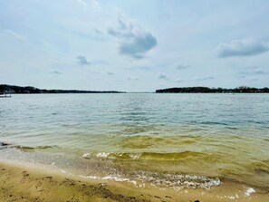 A beach with clear water, a sandy shore, and a distant tree line.