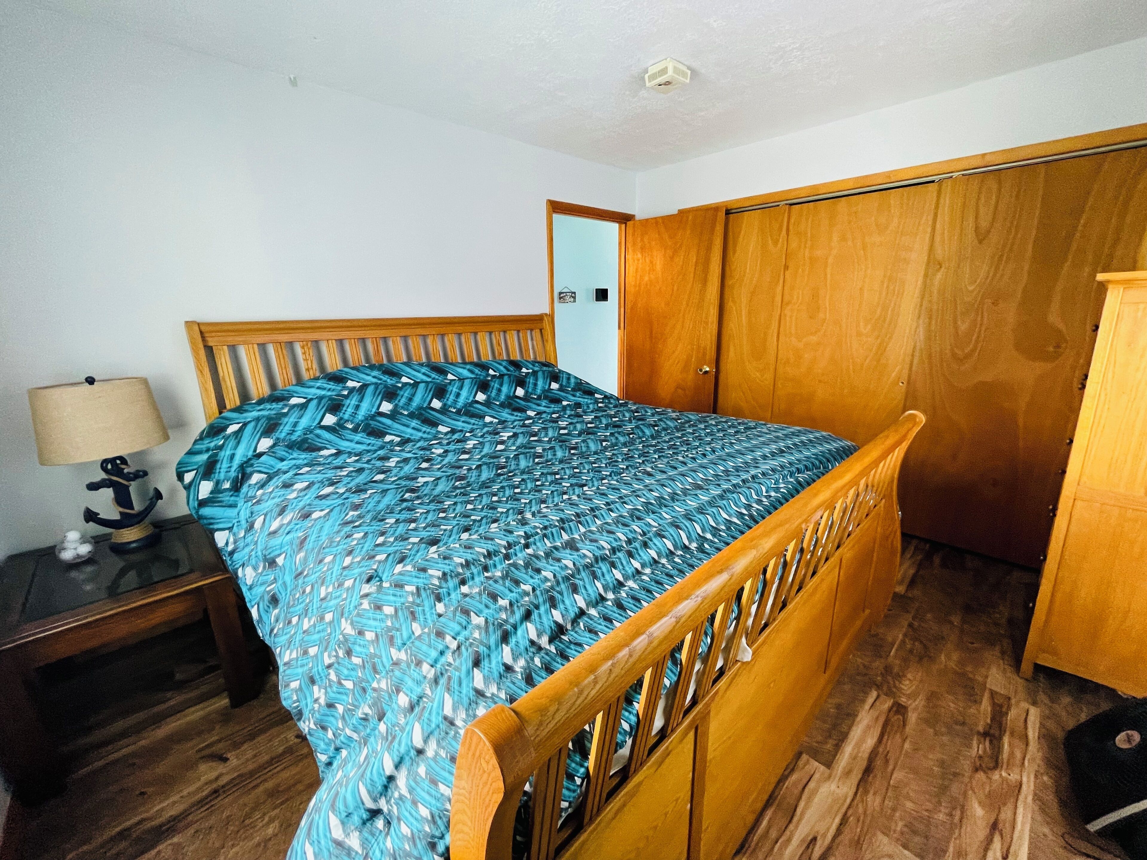 Een slaapkamer met een houten bed, een nachtkastje met een lamp en een kledingkast.