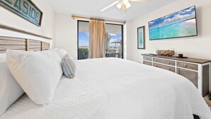 A bedroom with a large bed, a ceiling fan, a TV, and a view of the ocean. - Windward Pointe 104 with Beach Access (Orange Beach)