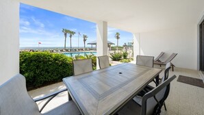 A covered outdoor dining area with a view of a pool and palm trees. - Windward Pointe 104 with Beach Access (Orange Beach)