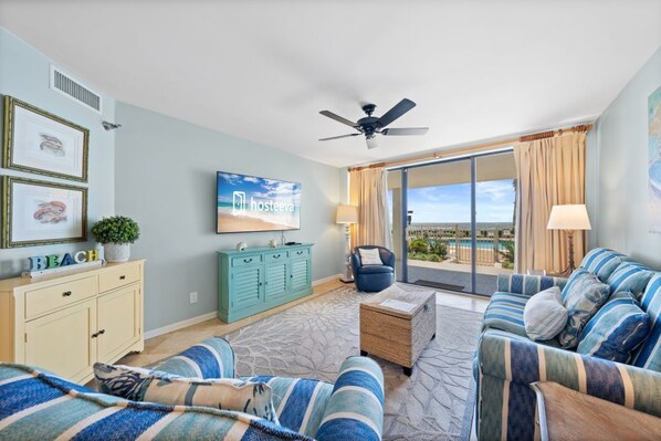 A hotel room with a large window, a ceiling fan, a television, a sofa, a small table, and a cabinet. - Windward Pointe 104 with Beach Access (Orange Beach)