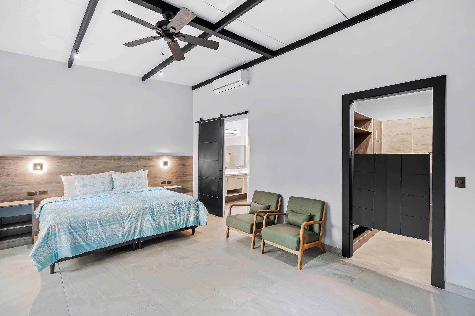 A modern bedroom with a bed, two chairs, a ceiling fan, and a wardrobe.