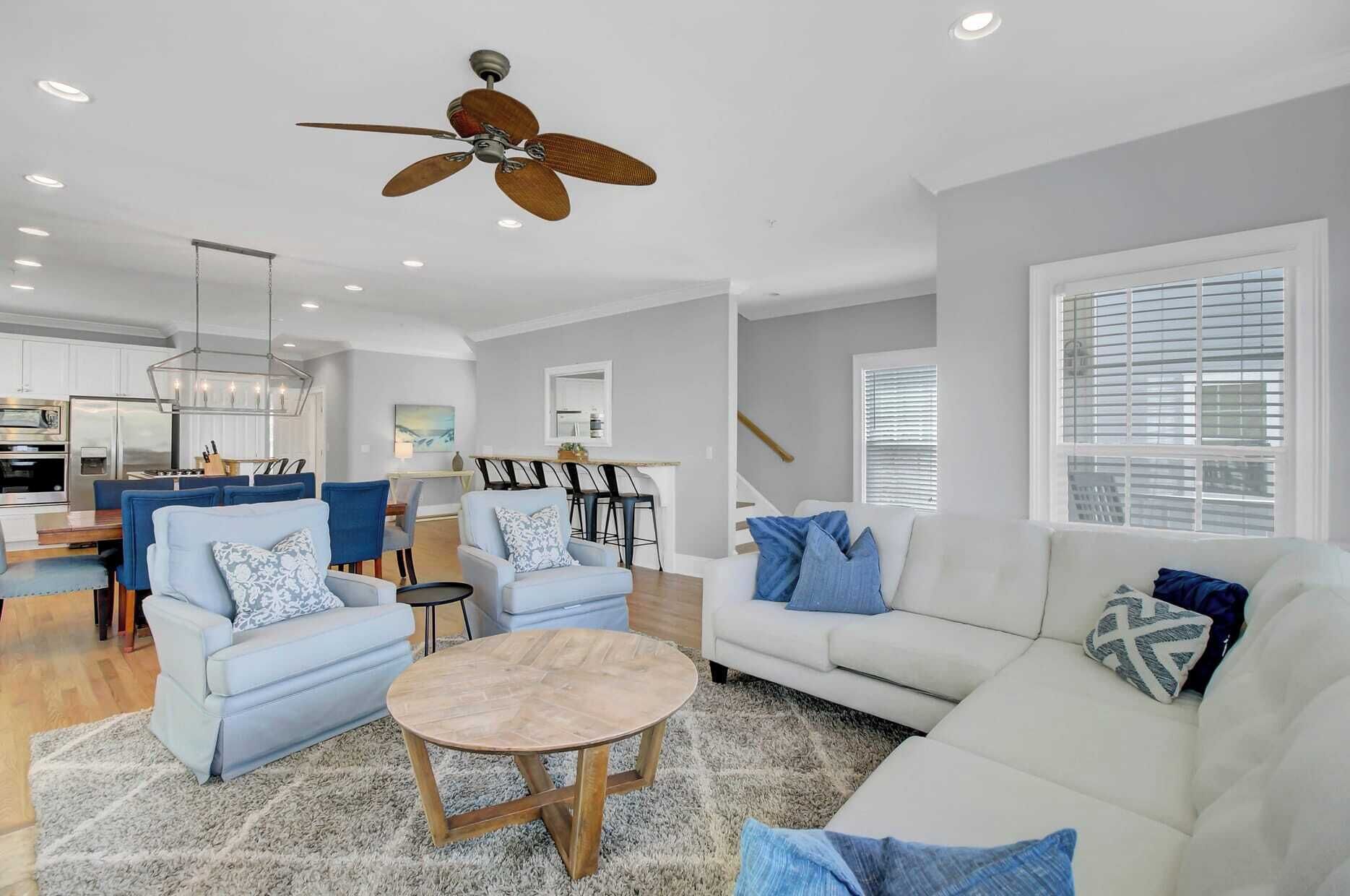Un salon moderne avec un canapé blanc, des fauteuils bleus, une table basse et un ventilateur de plafond.