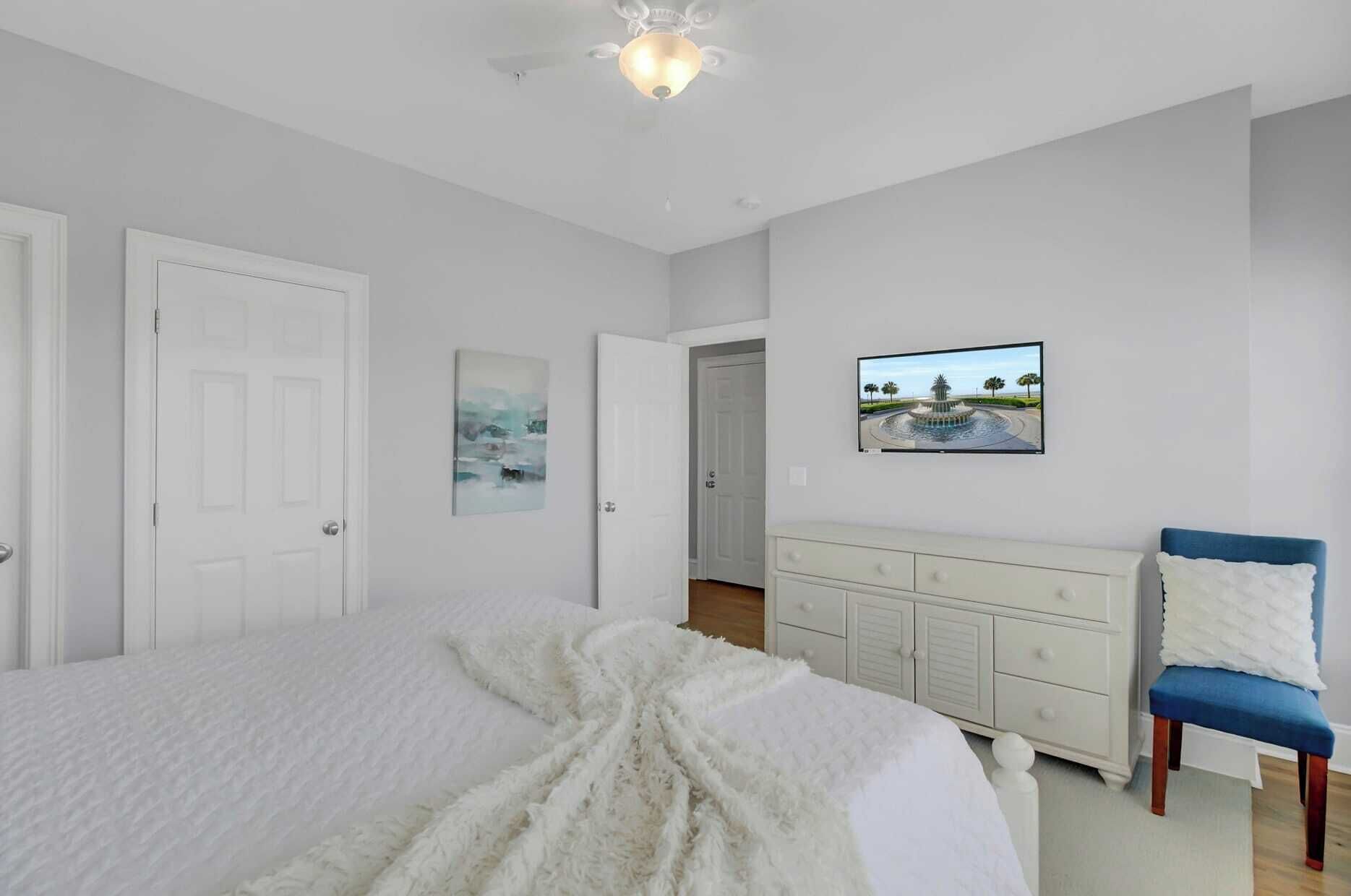 Een slaapkamer met een bed, een dressoir, een stoel en een plafondventilator.