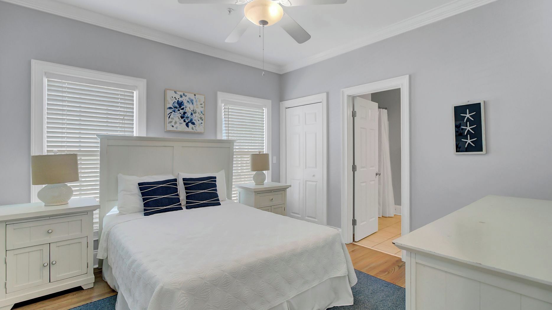 A bedroom with a bed, nightstands, a ceiling fan, and artwork on the walls.