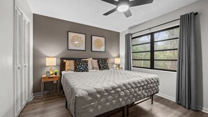 Un dormitorio con cama, lámparas de noche, ventilador de techo y ventana con cortinas.