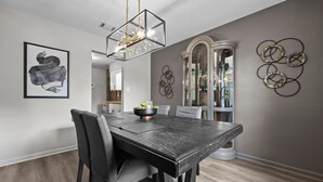 Un comedor con mesa de madera oscura, sillas, una lámpara de araña y decoración en la pared.