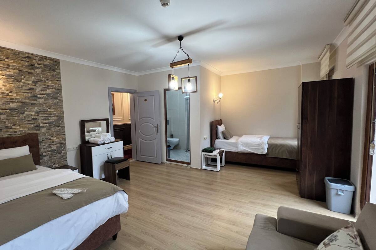 A hotel room with a bed, a desk, a chair, a wardrobe, and a bathroom visible through an open door.