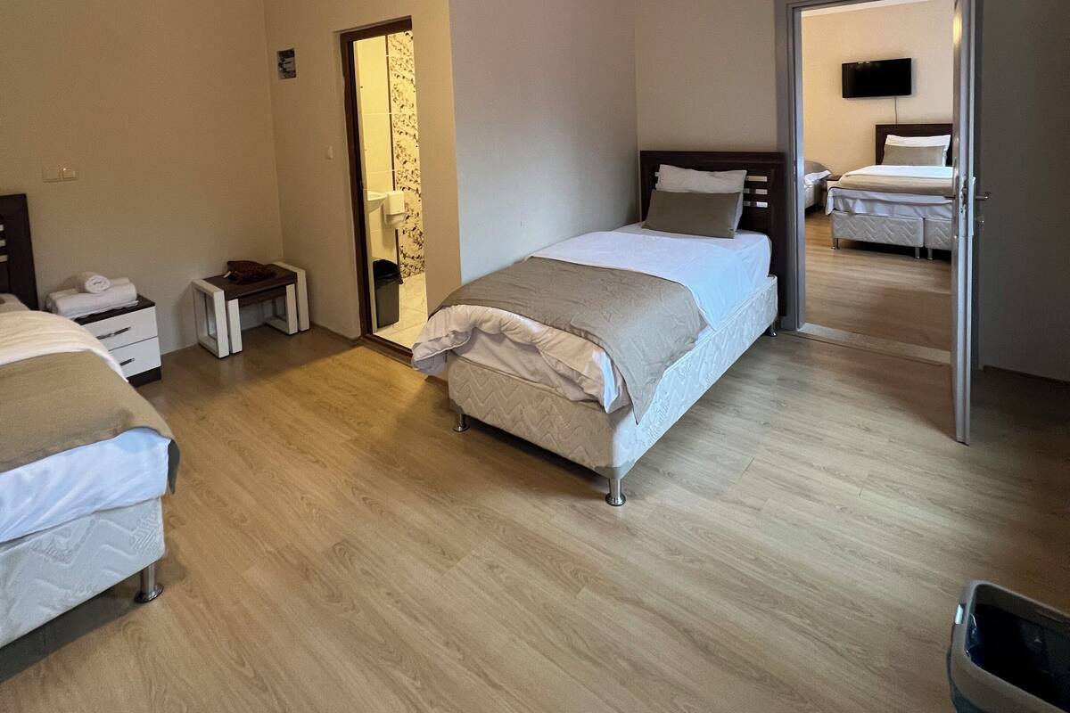 A modern hotel room with a large bed, a bedside table, a small desk, and a wardrobe. There is a bathroom visible through an open door.