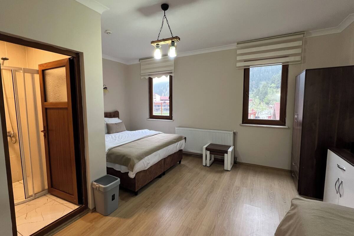 A bedroom with a bed, a small bedside table, a radiator, a window, a wardrobe, and a door leading to a bathroom.