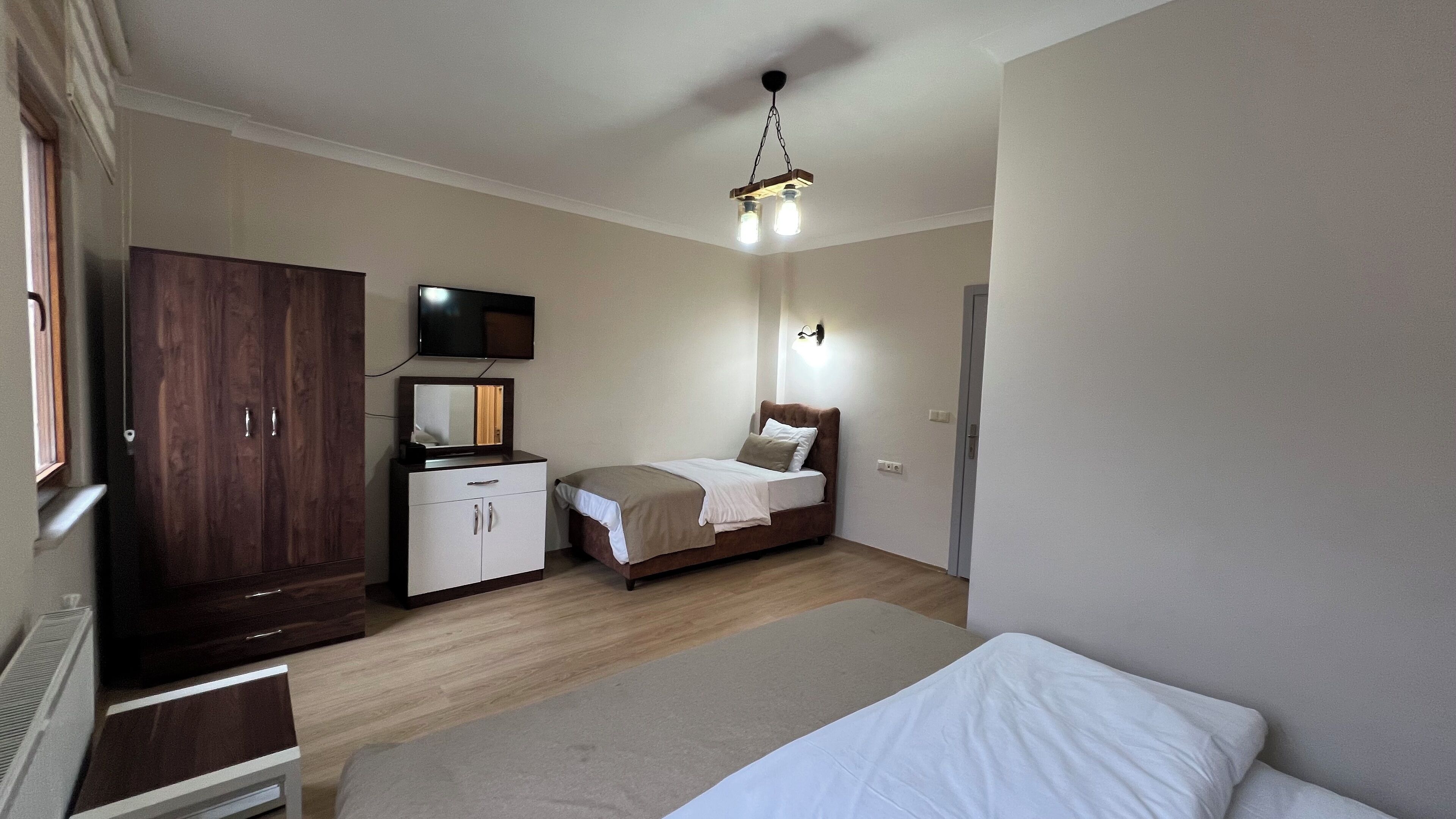 A bedroom with a bed, a wardrobe, a desk, a television, and a wall-mounted light fixture.