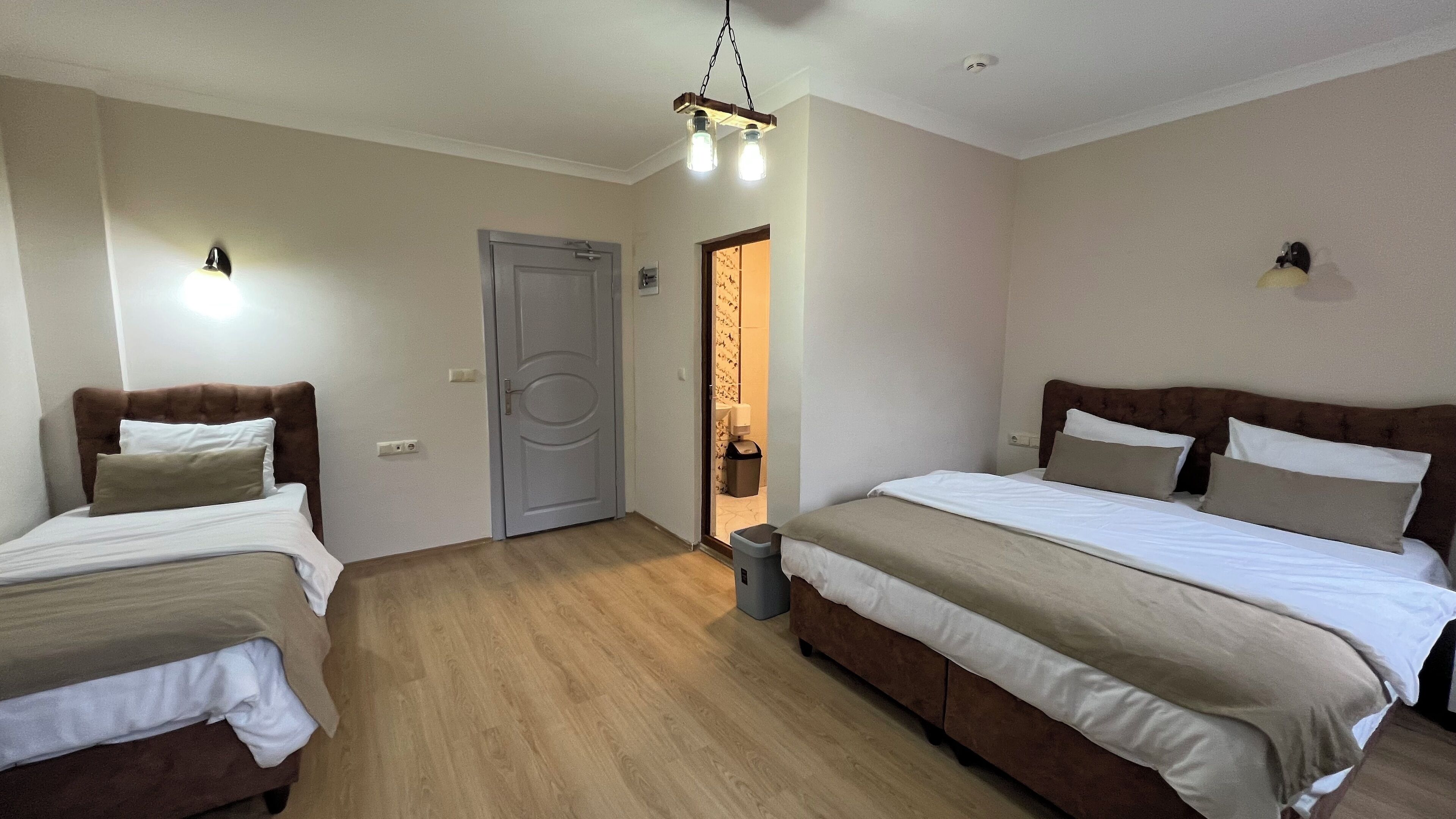 A hotel room with two beds, a wooden floor, a door, and a trash bin.