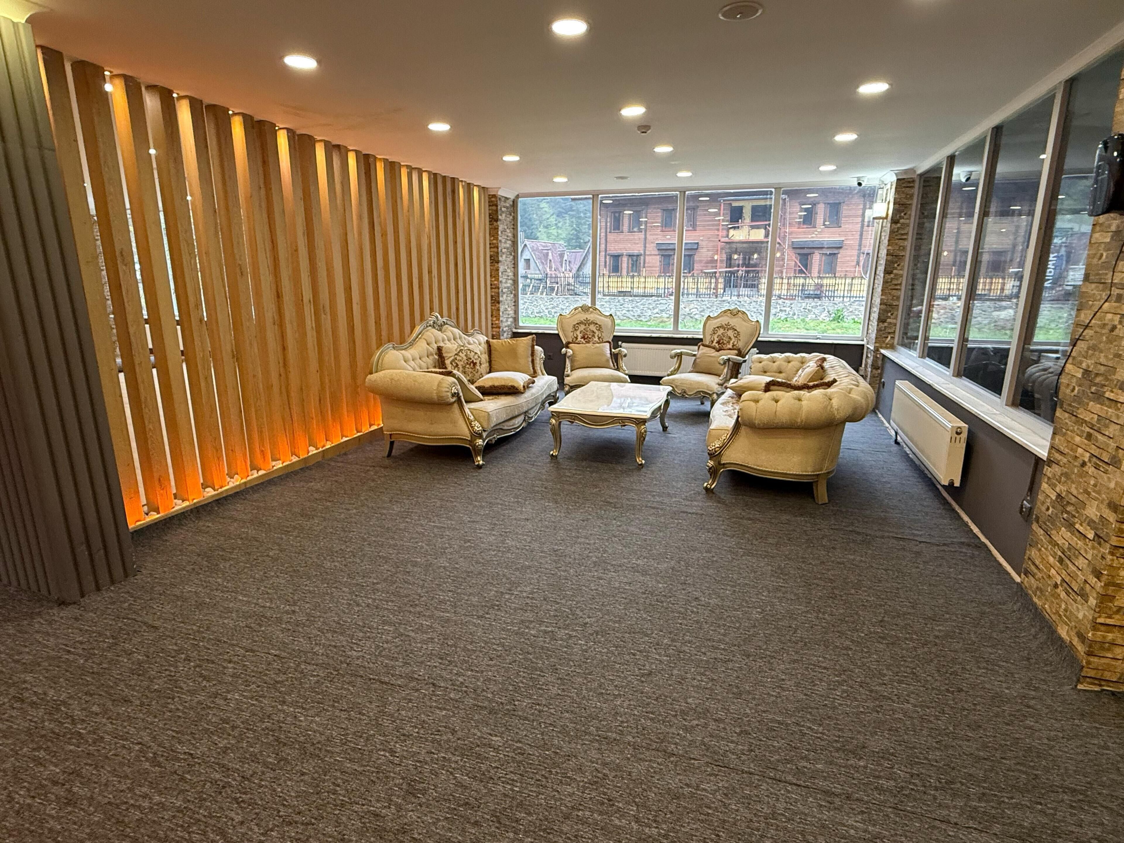 A room with a sofa set, armchairs, and a coffee table, with a view of buildings through large windows.