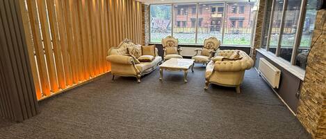 A room with a sofa set, armchairs, and a coffee table, with a view of buildings through large windows.