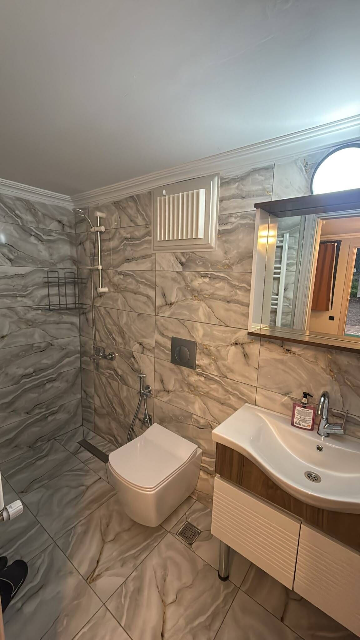 A modern bathroom with a marble wall, a walk-in shower, a freestanding bathtub, and a vanity with a mirror.