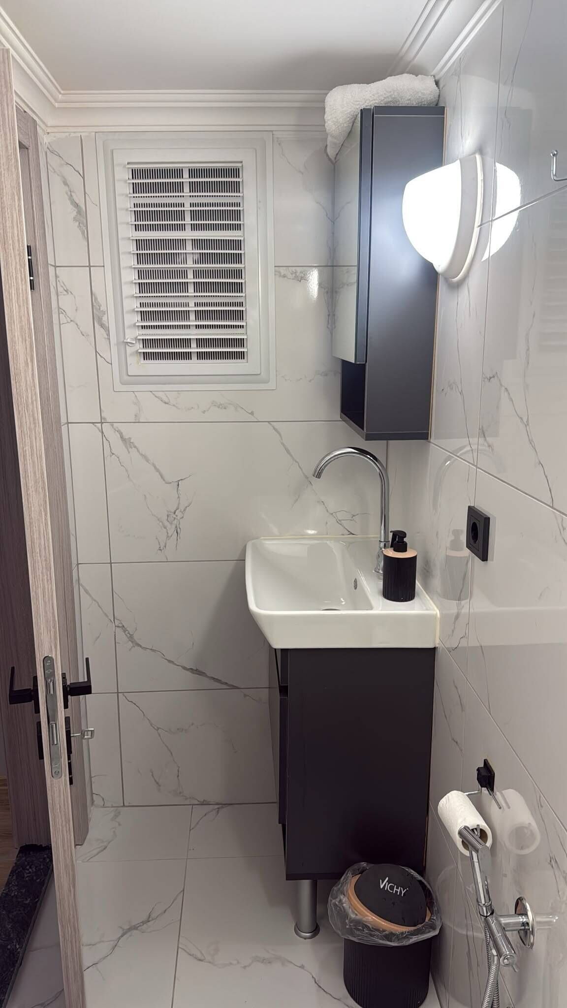 A bathroom with a white sink, dark cabinet, and a window with blinds.