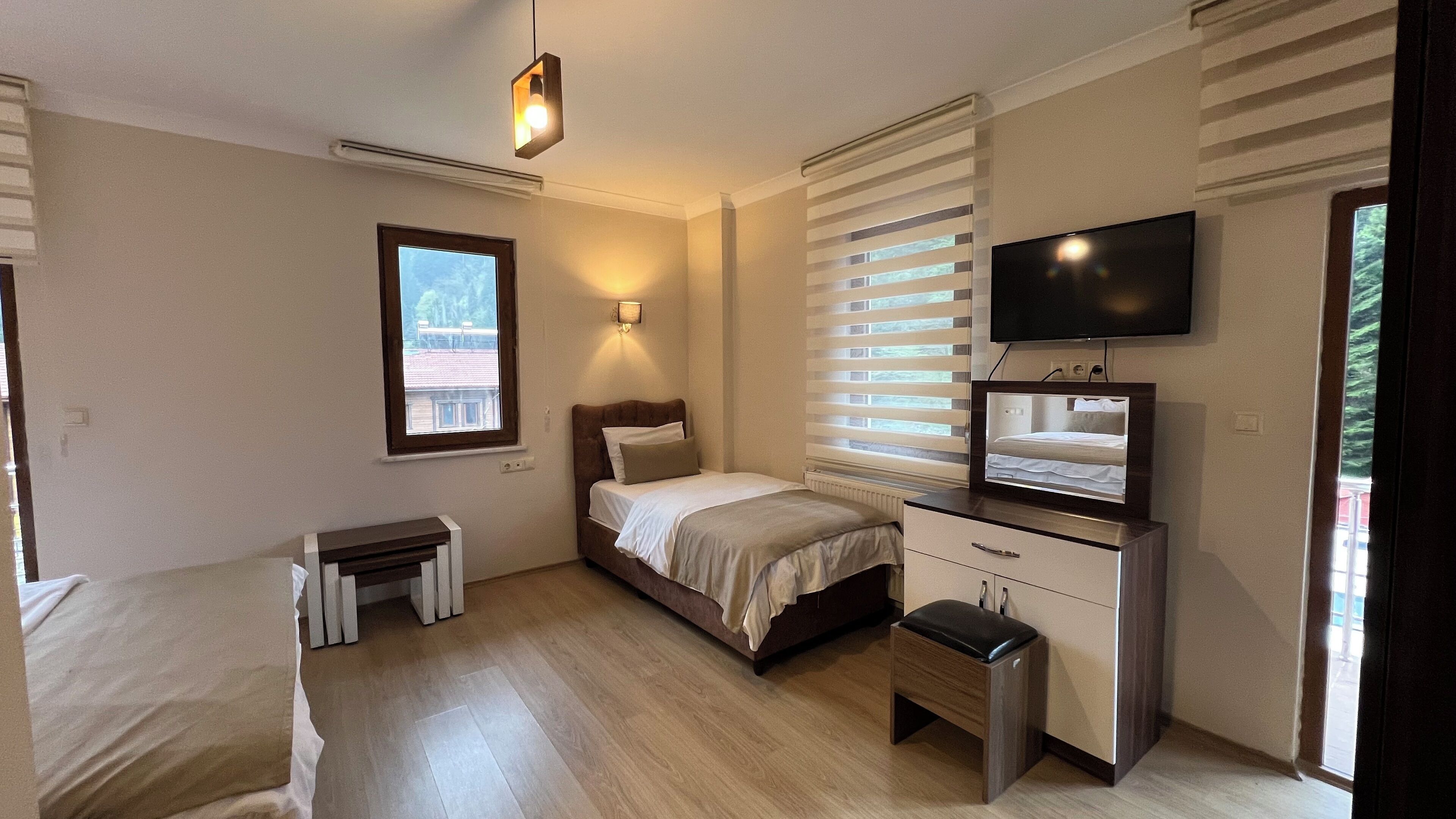 A bedroom with a bed, bedside table, dresser, TV, and window with blinds.