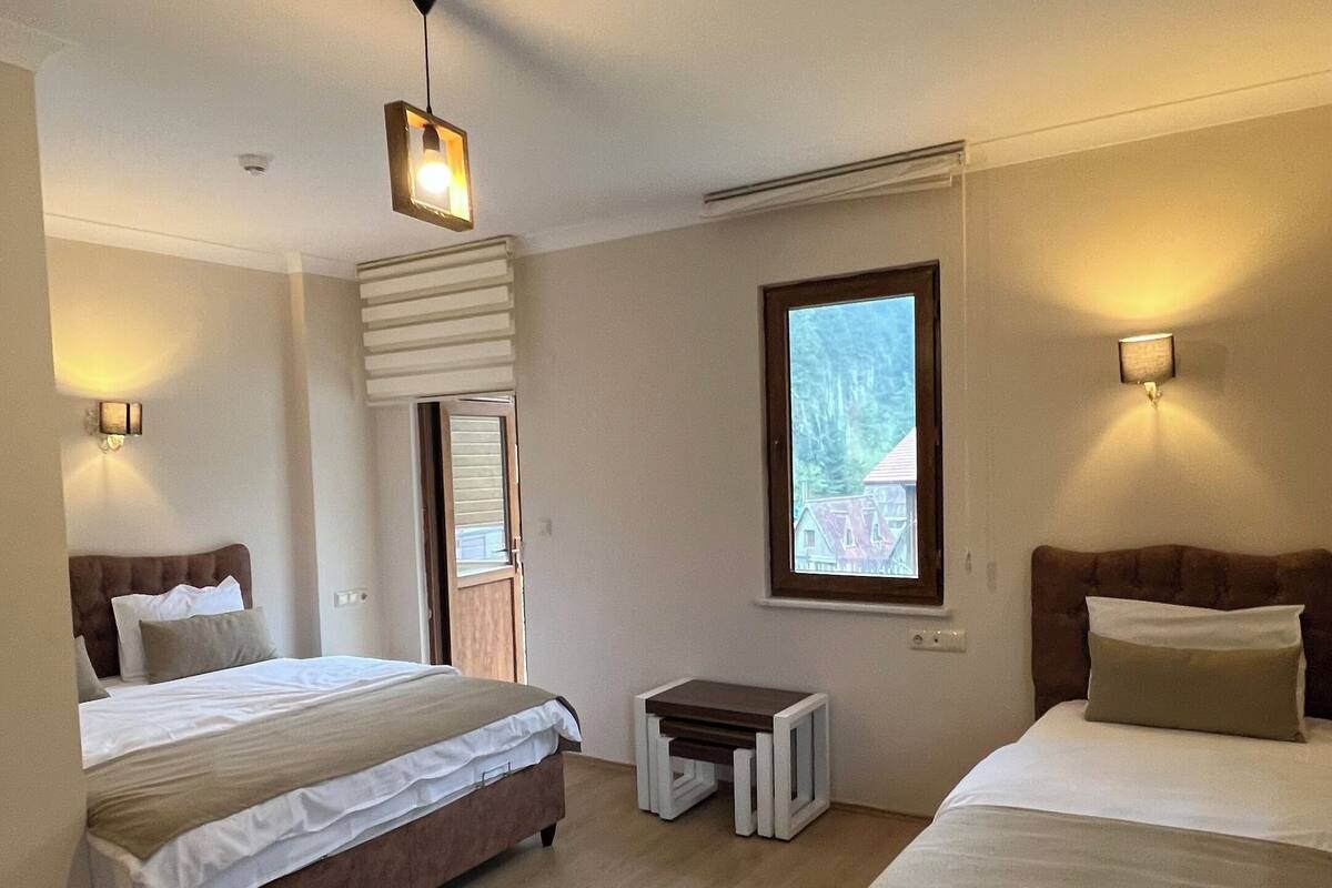 A hotel room with two beds, a small table, and a window with a view.