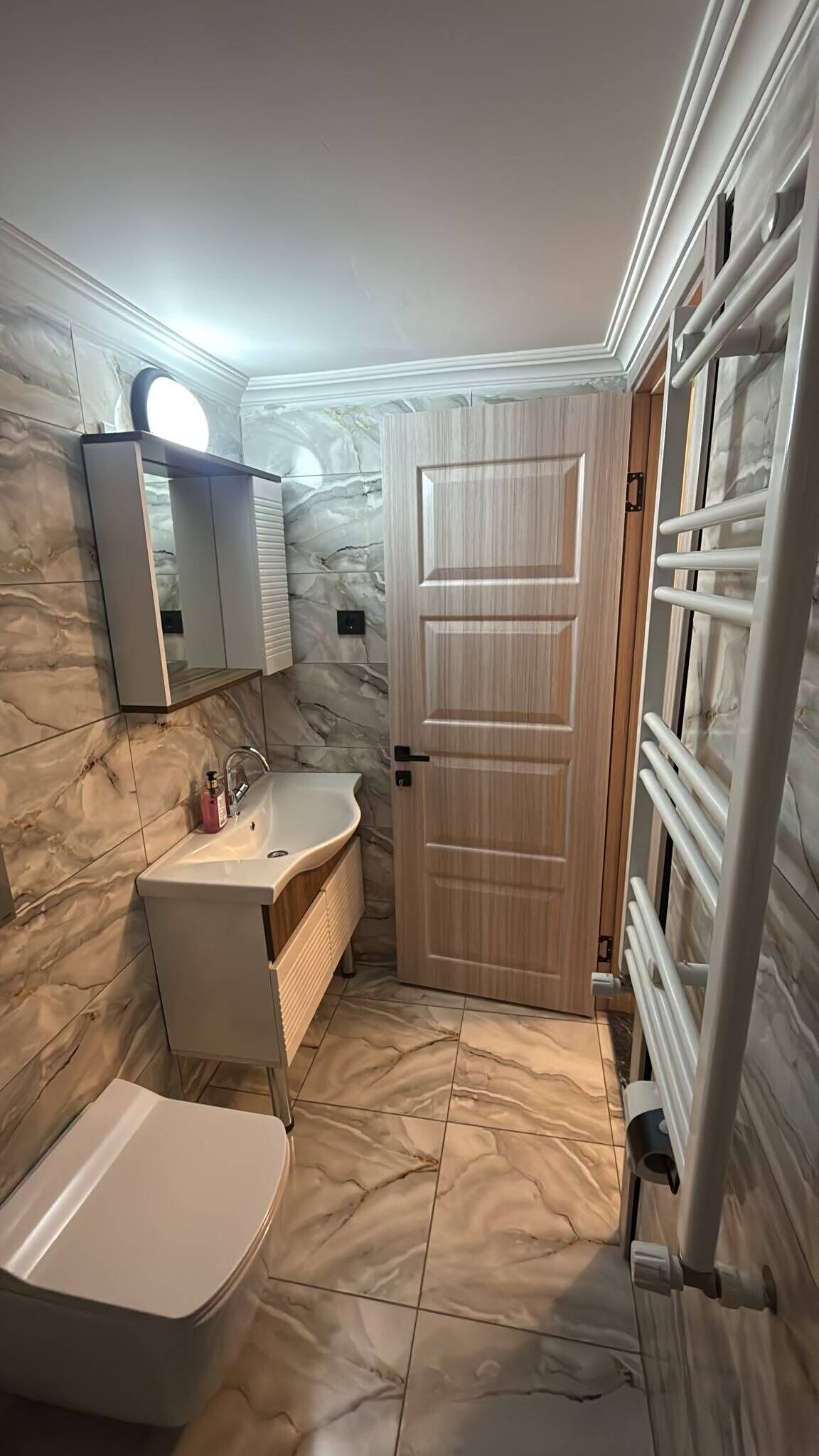 A bathroom with a marble floor, a sink, a toilet, a mirror, and a door.