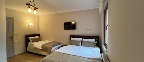 A hotel room with two beds, a TV mounted on the wall, and a ceiling light fixture.
