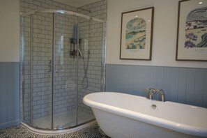 A bathroom with a glass-enclosed shower, a freestanding bathtub, and two framed artworks on the wall. - The Old Farmhouse (Truro)