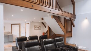 Ein großzügiger Wohnbereich mit einem großen, schwarzen Ledersofa, einer Holztreppe und Blick auf die Küche im Hintergrund.