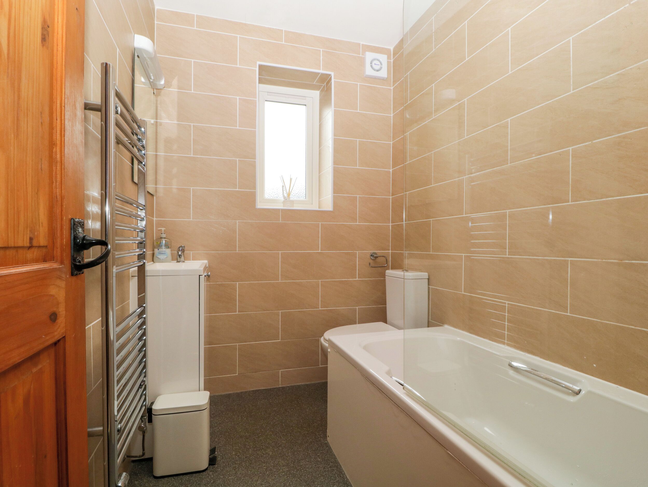A bathroom with beige tiles, a bathtub, a toilet, a sink, and a window.