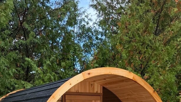 Een houten sauna met een gebogen buitenkant, twee banken binnenin en een glazen deur.