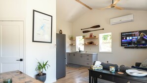 Een moderne keuken met een koelkast, houten kastjes, een eettafel en een televisie waarop een muziekvideo afspeelt.