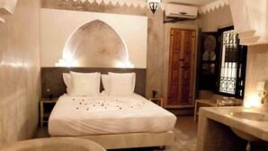 A bedroom with a large bed, a bathtub with rose petals, a wooden door, and a chandelier. - Spacious 5-bedroom riad in charming Marrakesh with AC, WiFi and Pool (Marrakesh)