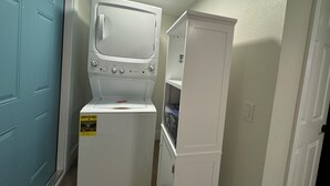 A compact laundry room with a front-loading washer and dryer, a blue door, and a white cabinet.