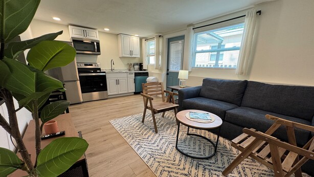 A modern living room with a grey sofa, wooden chairs, a coffee table, and a kitchen in the background.