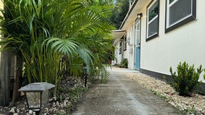 A pathway leading to a building with a blue door, surrounded by lush greenery and a small garden area.