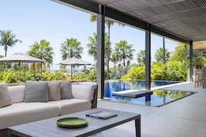 Un área de estar moderna al aire libre con piscina, palmeras y vistas despejadas del océano.