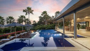 A modern outdoor pool area with lounge chairs and umbrellas, surrounded by palm trees and a clear sky. - Lagos del Mar (Punta de Mita)