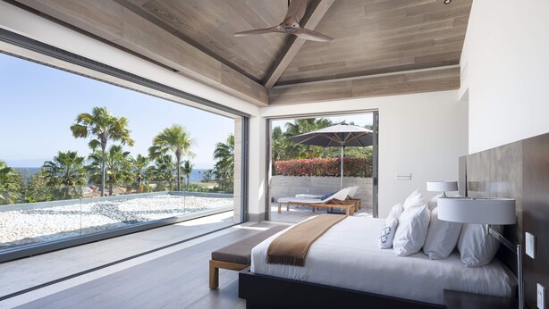 A modern bedroom with a large bed, a ceiling fan, and a view of the beach. - Lagos del Mar (Punta de Mita)