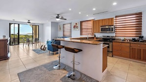 A modern kitchen with a central island, stainless steel appliances, and wooden cabinets. - Modern Penthouse w/ Sweeping Ocean Views & Beach Club Access (Coco)