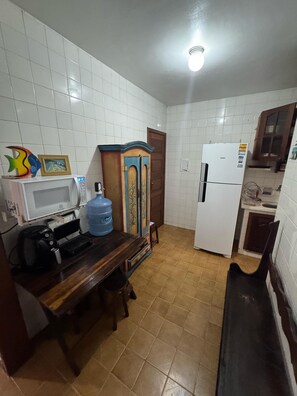 Eine kleine Küche mit hell geflieste Wänden, einem Holzkorpus, einem weißen Kühlschrank und einer Mikrowelle auf einem kleinen Tisch.
