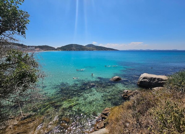 Eine Küstenlandschaft mit klarem türkisblauem Wasser, felsigen Ufern und sanften Hügeln im Hintergrund.