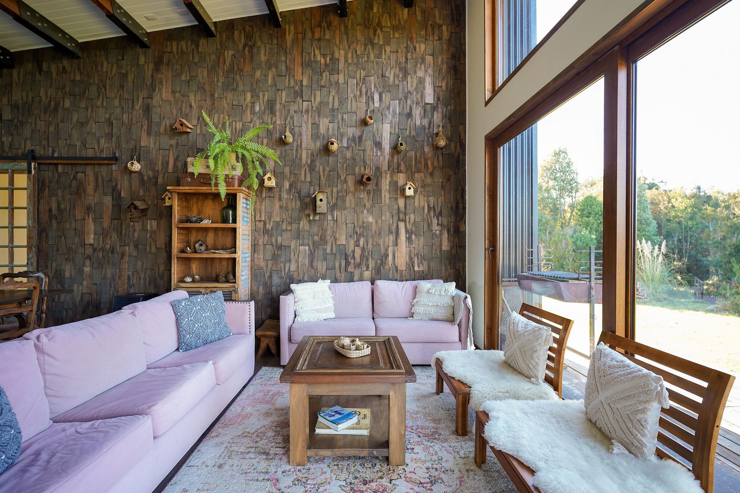 Una sala de estar acogedora con una pared de madera, un sofá rosa, una mesa de centro de madera y vistas a través de un ventanal.