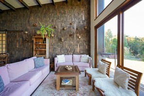A cozy living room with a wooden wall, a pink sofa, a wooden coffee table, and a view through a large window. - Oceana Suites Altos de Neoalerce (Puerto Montt)