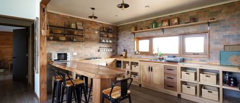 Une cuisine avec un îlot central en bois, des tabourets de bar, un four à micro-ondes et un mur en briques.