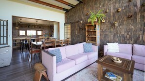 Un vaste espace de vie doté d’un plafond en bois, d’un canapé rose, d’une table basse et d’un coin repas avec des chaises et une table.