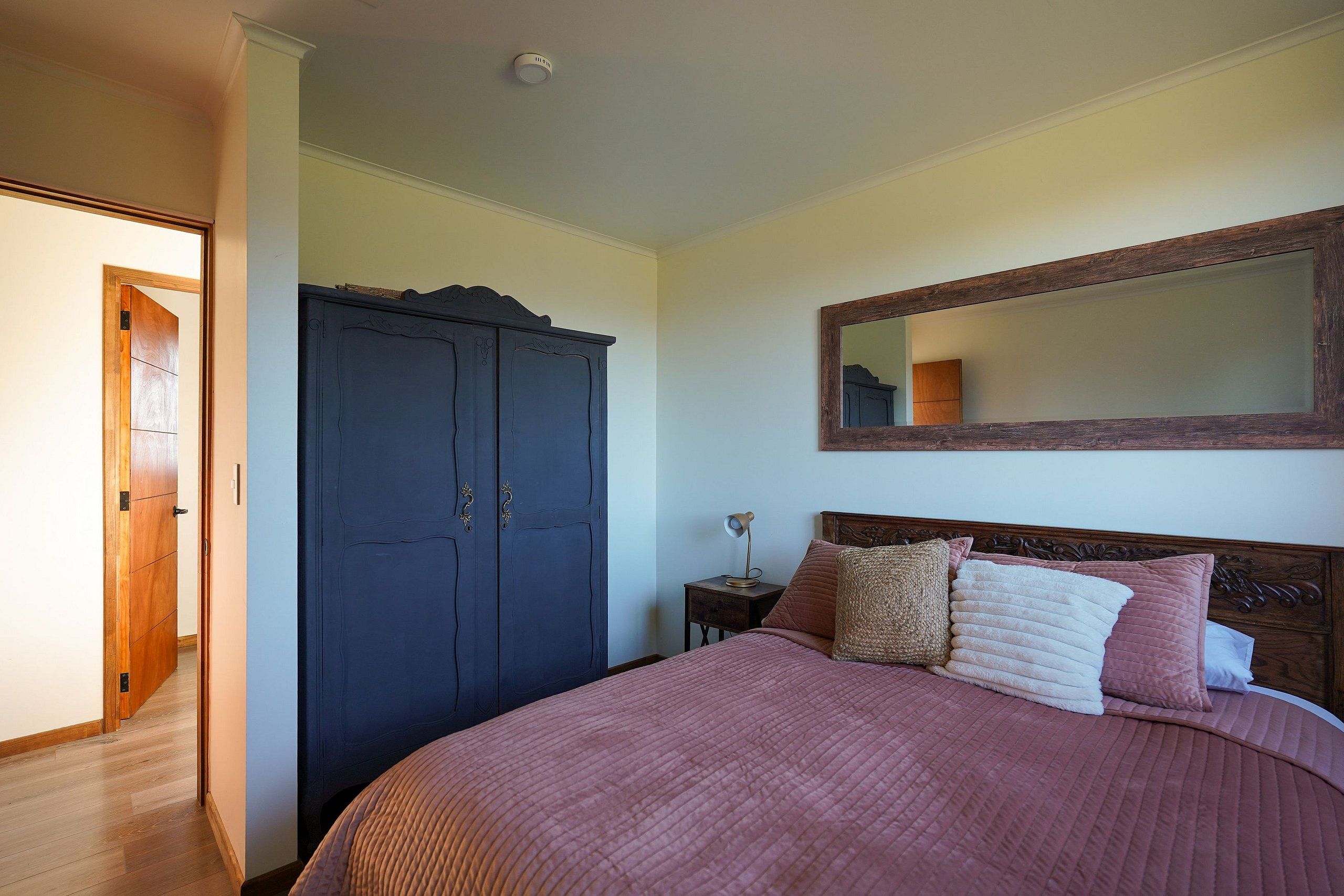 A bedroom with a large bed, a wardrobe, a nightstand, and a mirror on the wall.